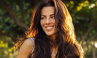 Smiling woman with long, glossy dark hair photographed outdoors in natural light.