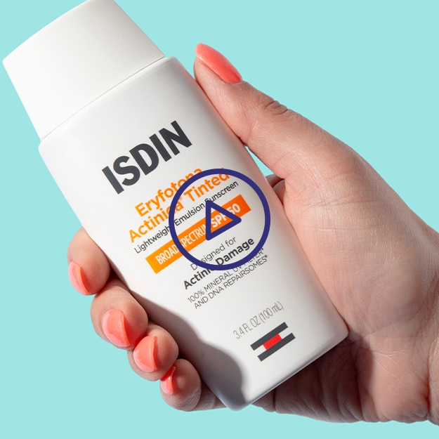 Manicured hand holding the new ISDIN Eryfotona Actinica Tinted on a light teal background.