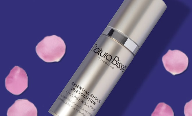 Silver skincare bottle with pink petals on a purple background.