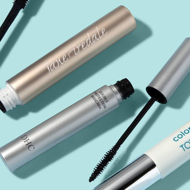 Three tubing mascaras including jane iredale with one wand uncapped to show the brush on a mint background.