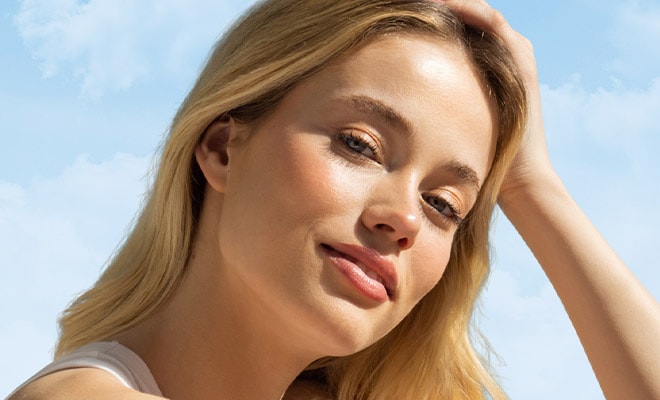 Young, blonde-haired woman smiling and resting her head on her hand.