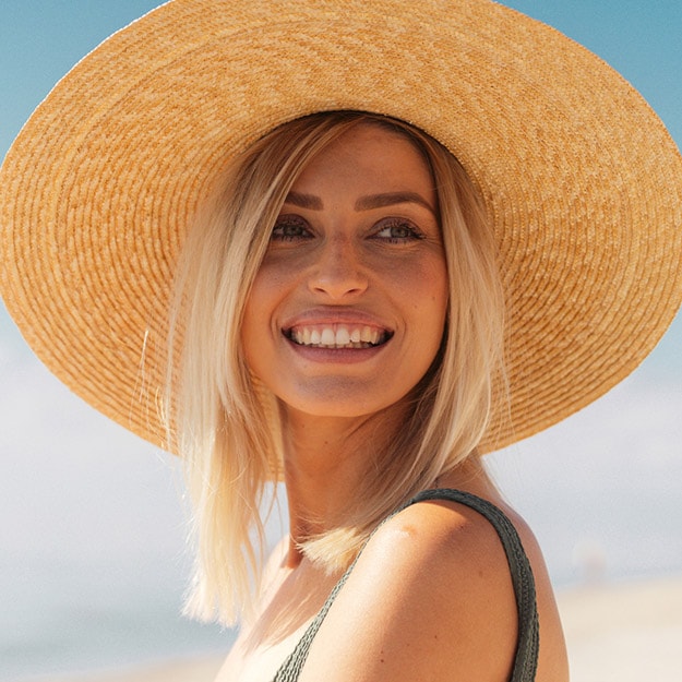 Model smiling and wearing a wide brimmed hat in the sun.