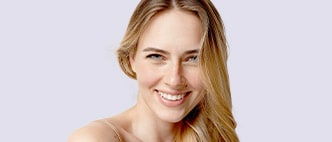 Smiling woman with long, healthy-looking blonde hair set against a soft background.