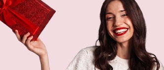 Smiling woman with red lipstick in a cream sweater against a light pink background.