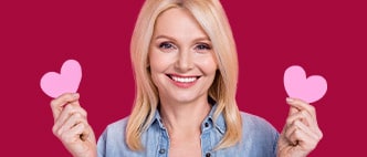 Smiling woman holding pink paper hearts for Valentine's Day gift guide on a magenta background