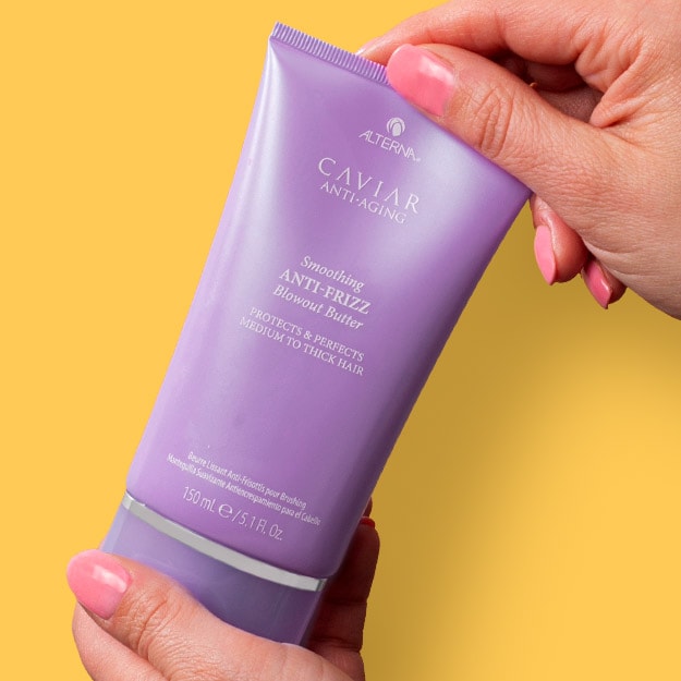 Hand holding Alterna Caviar Anti-Aging hair styling product in purple tube