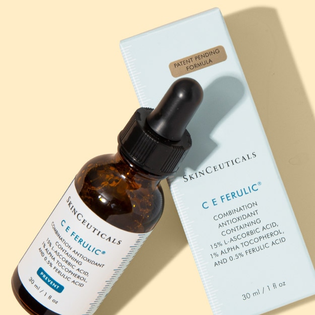 SkinCeuticals C E Ferulic dropper bottle leaning against its carton on a pale yellow background.