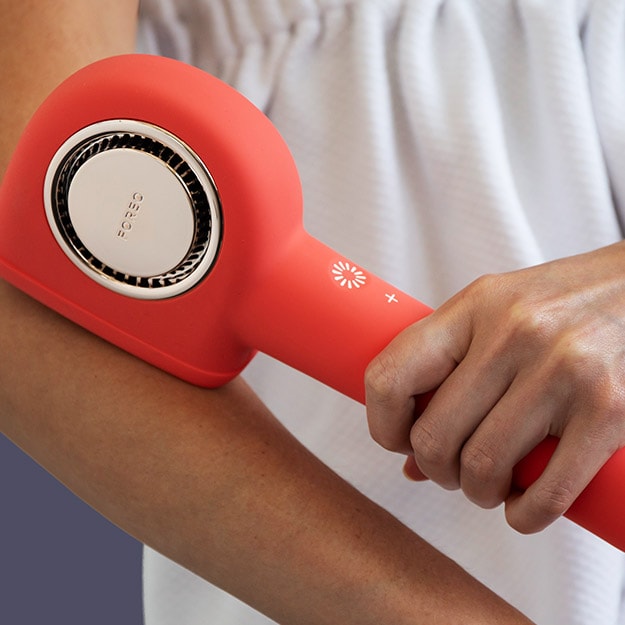 Person gliding a red handheld skin care device along their forearm.