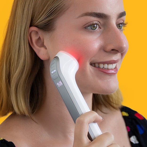 Woman holding a red light therapy wand against her cheek on a light background.