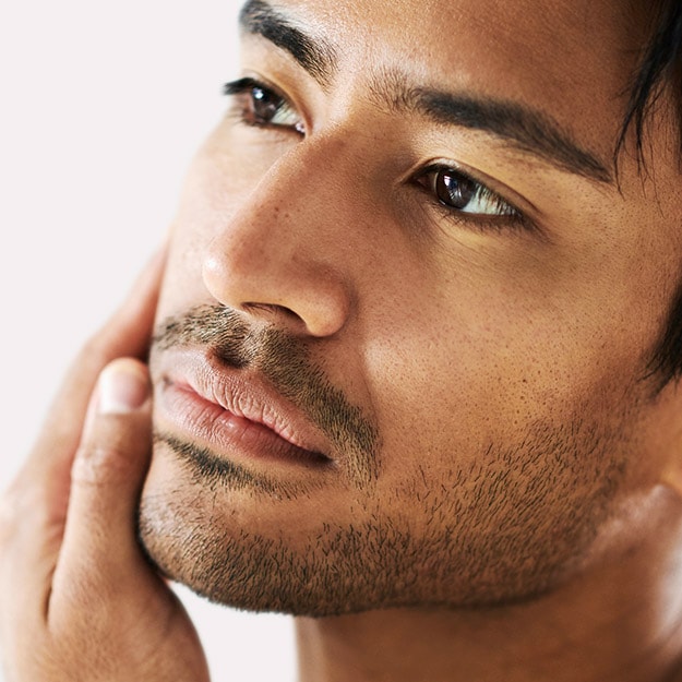 Man with short stubble touching his cheek and jawline after shaving.