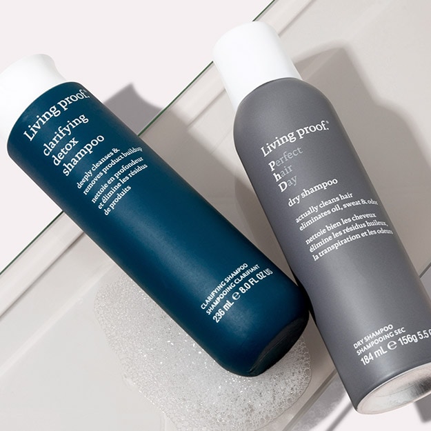 Living Proof Clarifying Detox Shampoo and Perfect hair Day Dry Shampoo resting on a tub ledge.
