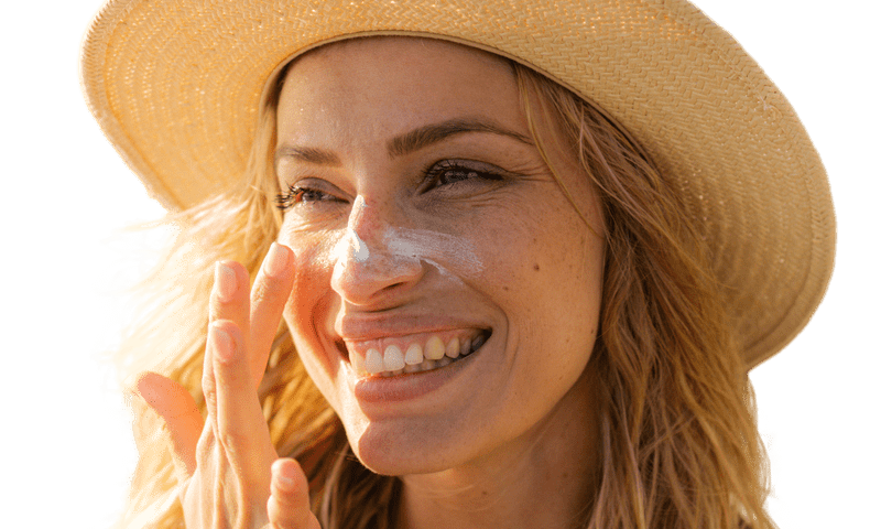 Smiling young woman wearing a sunhat and applying sunscreen to her face.